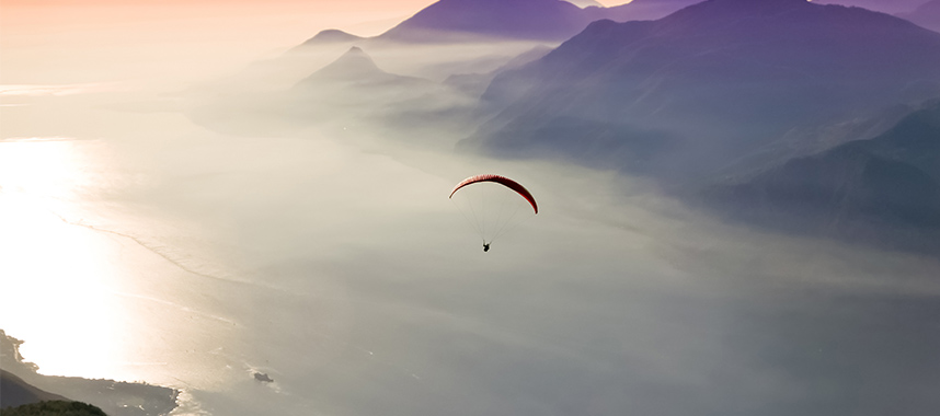 Man in a parachute flying over a peaceful valley at dawn