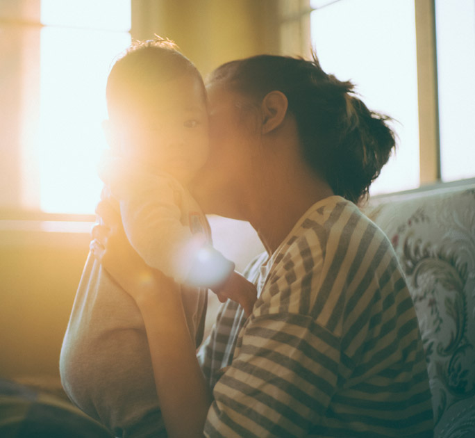 A mother kisses her baby amidst the setting sun