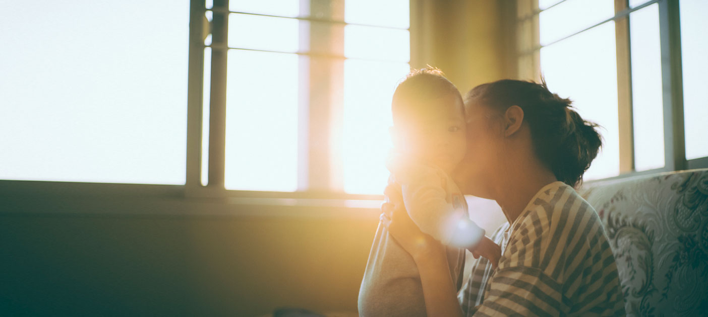 A mother kisses her baby amidst the setting sun