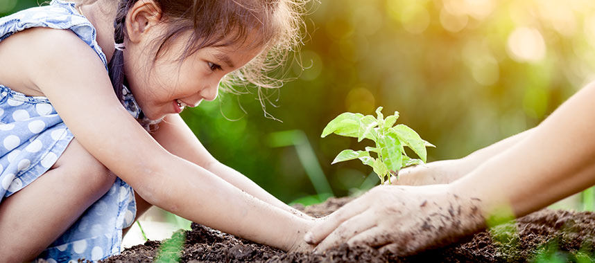 A parent guides her daughter's hands as they plant a seedling together