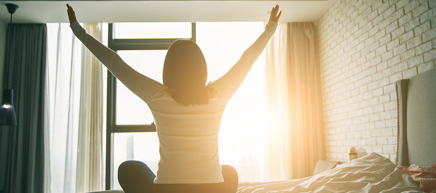 Young woman stretching on her bed in the early morning